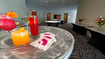 A table with three drinks, a vase with flowers, and a sign with a logo.