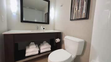 A bathroom with a white toilet, a dark brown vanity, a mirror, and a framed artwork on the wall.