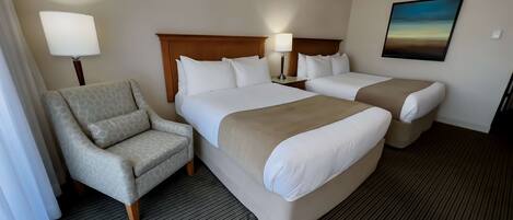 Habitación de hotel con dos camas, una silla, una lámpara y un cuadro en la pared.