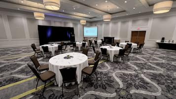 A conference room with multiple round tables and chairs, a large screen, and a podium.