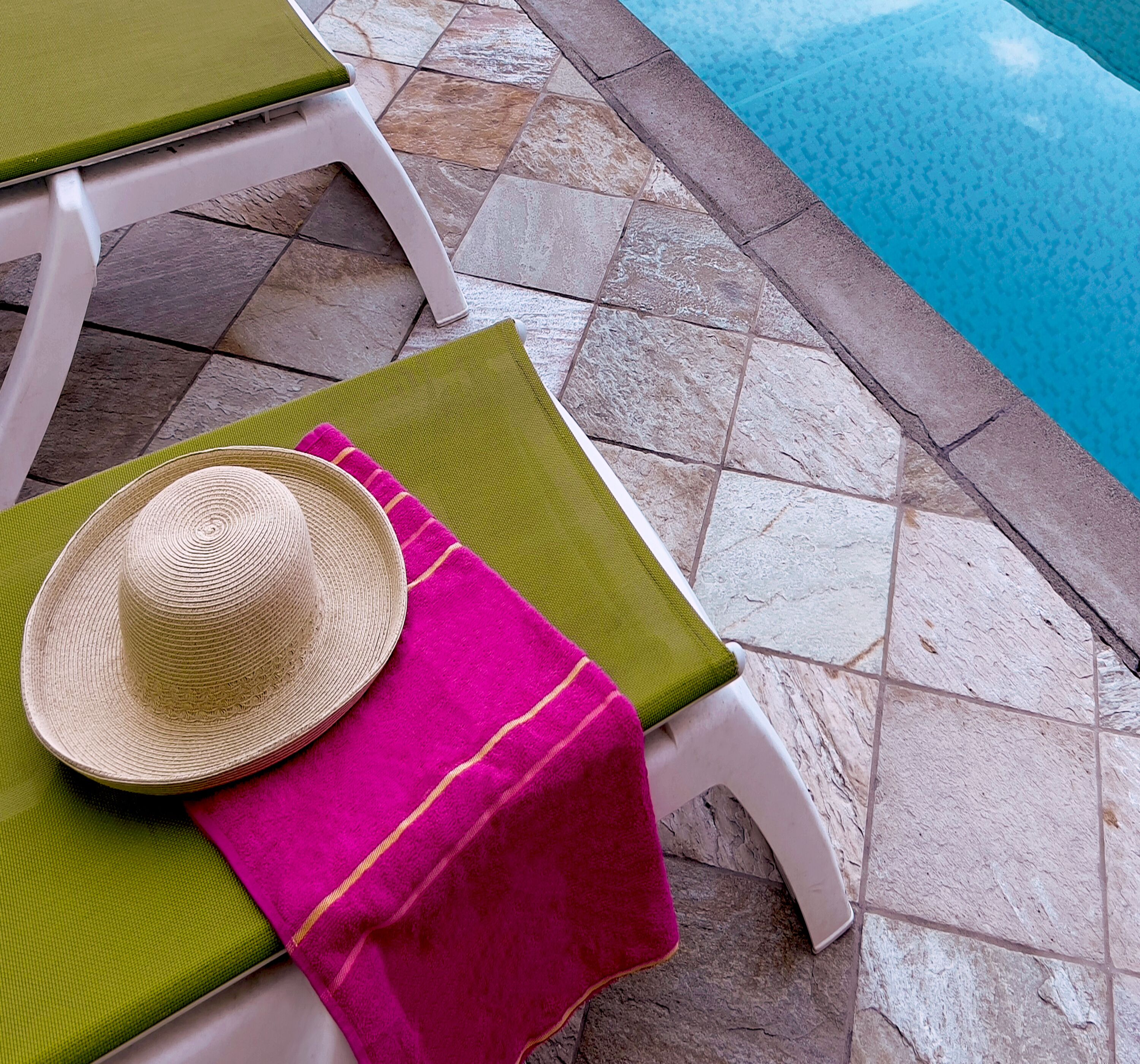 A poolside area with a lounge chair, a hat, and a pink towel.