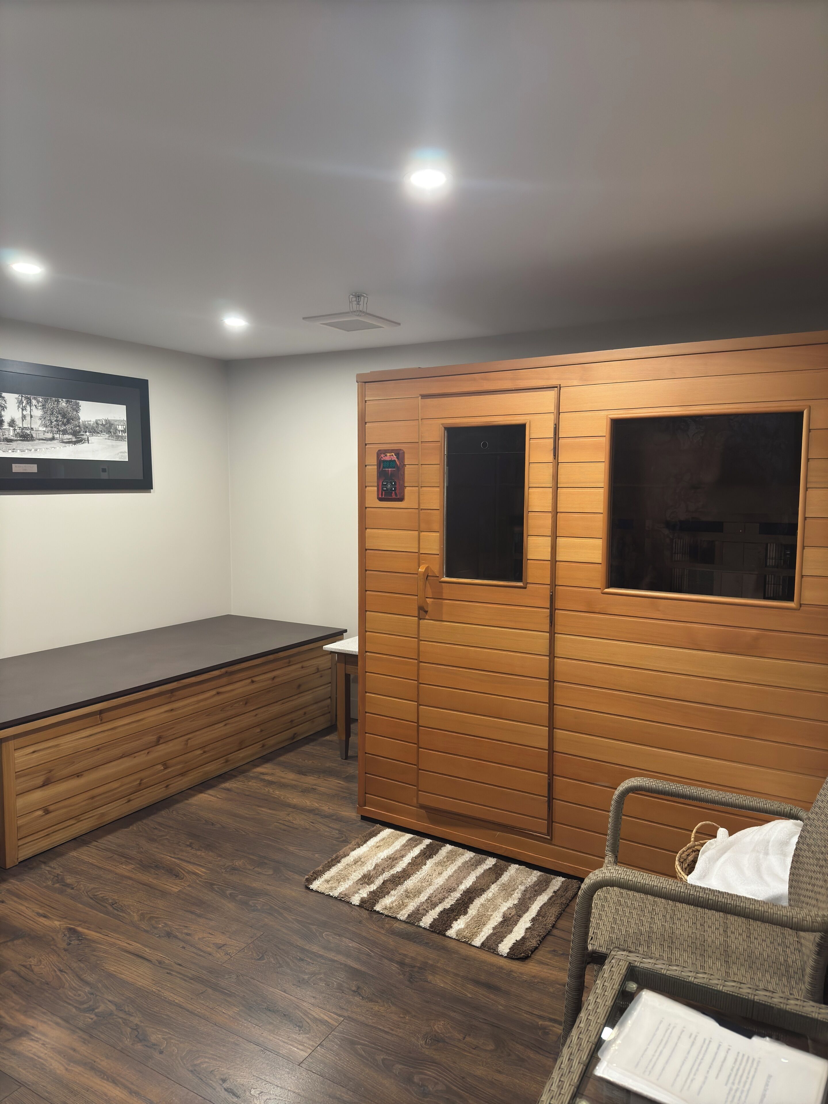A room with a wooden wardrobe, a bench, a wicker chair, and a framed picture on the wall.