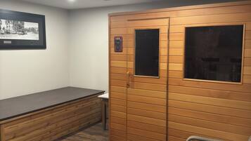 A room with a wooden wardrobe, a bench, a wicker chair, and a framed picture on the wall.