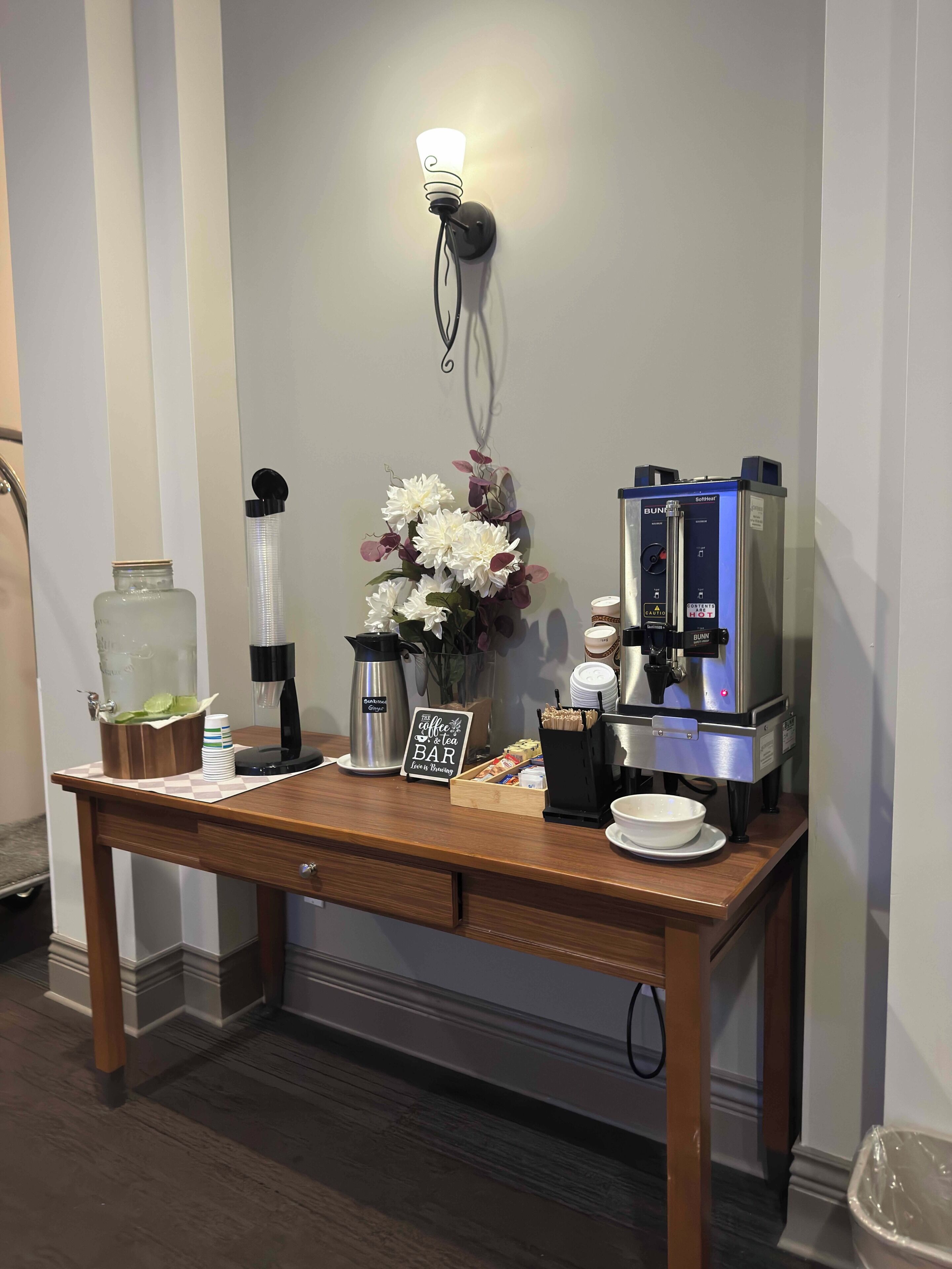 Een koffiehoek met een Bunn espresso machine, een waterdispenser, een koffiepot, een bloemstuk en een bordje dat aangeeft dat het een bar is.