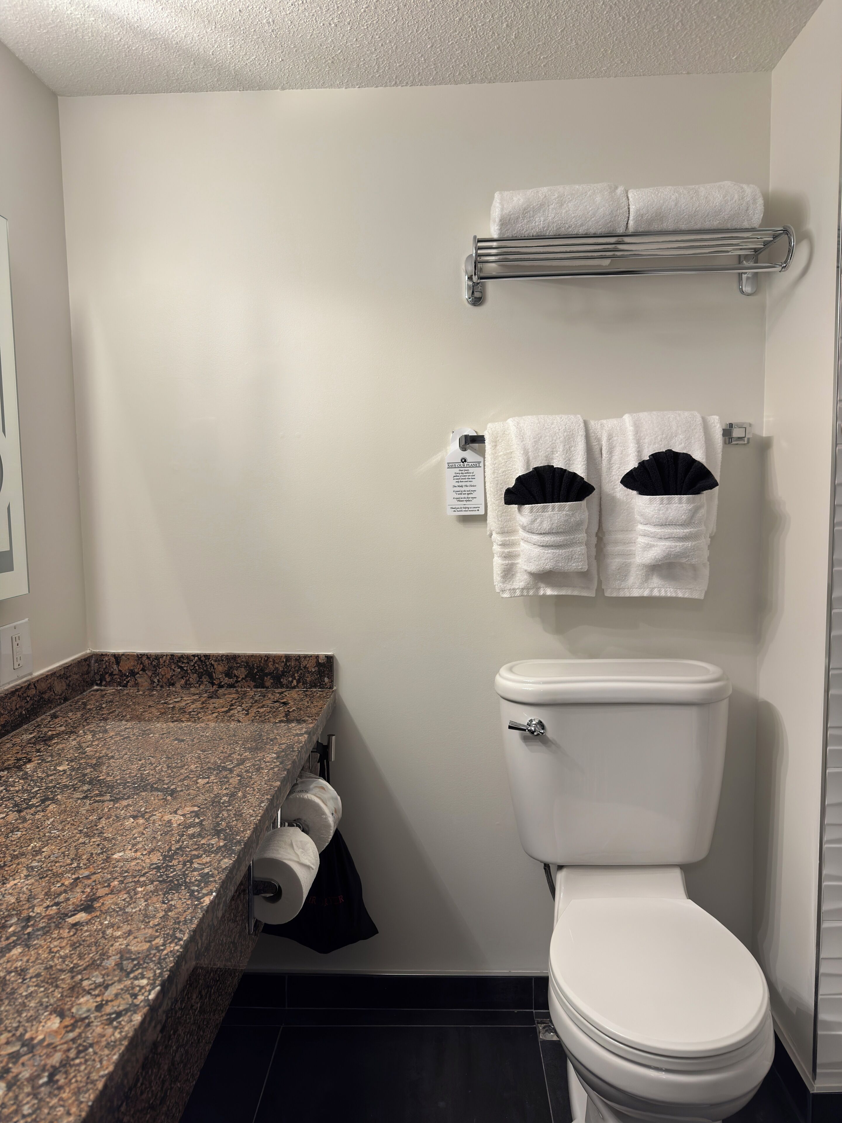 Un baño con inodoro, un perchero con dos toallas, dispensador de toallas de papel y encimera de granito.