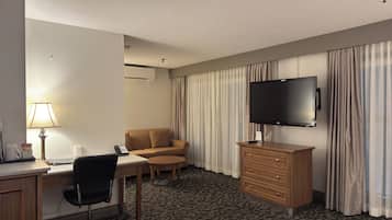 Hotellihuone, jossa on työpöytä, tuoli, sohva, televisio ja kuviollinen matto.