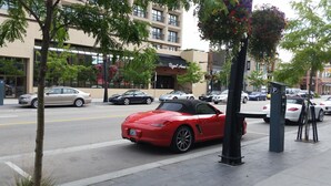 Un coche deportivo rojo estacionado en una calle de la ciudad, con edificios y árboles al fondo.