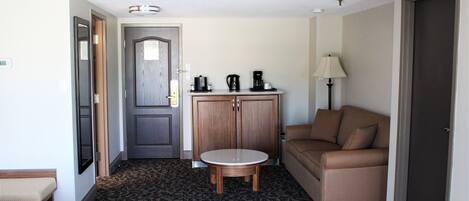 Une chambre d’hôtel comprenant un lit, une table ronde, un canapé, un meuble avec des machines à café et une lampe.