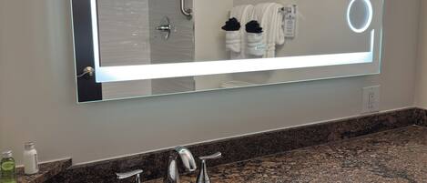 A bathroom with a large mirror, a sink, and a shower.
