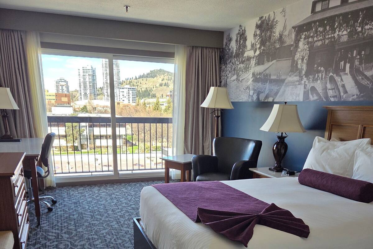 A hotel room with a large bed, a desk, a chair, and a view of the city through the window.