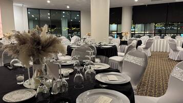A banquet hall with round tables set for a formal event, featuring white chairs with glittery sashes, black tablecloths, and clear glassware.