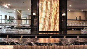 Zona de bar con una amplia pared de mármol iluminada, estantes con copas y una encimera de mármol pulido.