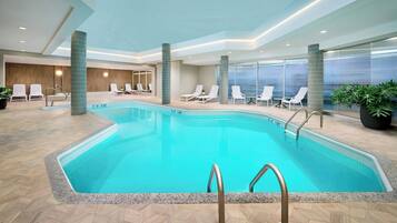 A swimming pool with lounge chairs, a wooden floor, and a view of the outside.
