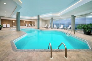 Una piscina con sillas de descanso, piso de madera y vista al exterior.