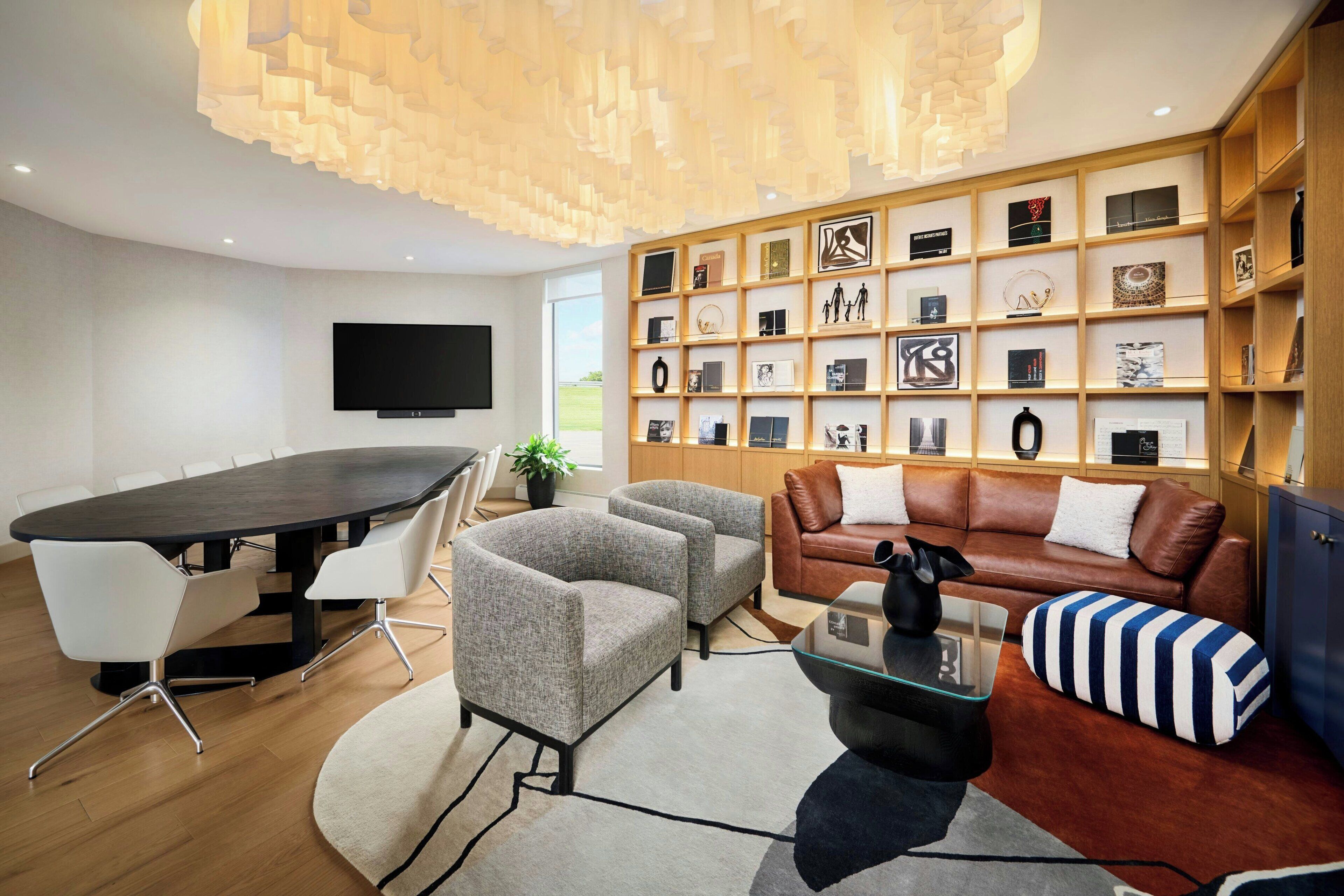 Una sala de estar moderna con una mesa redonda, dos sillones, un sofá, un televisor y una pared decorada con marcos.