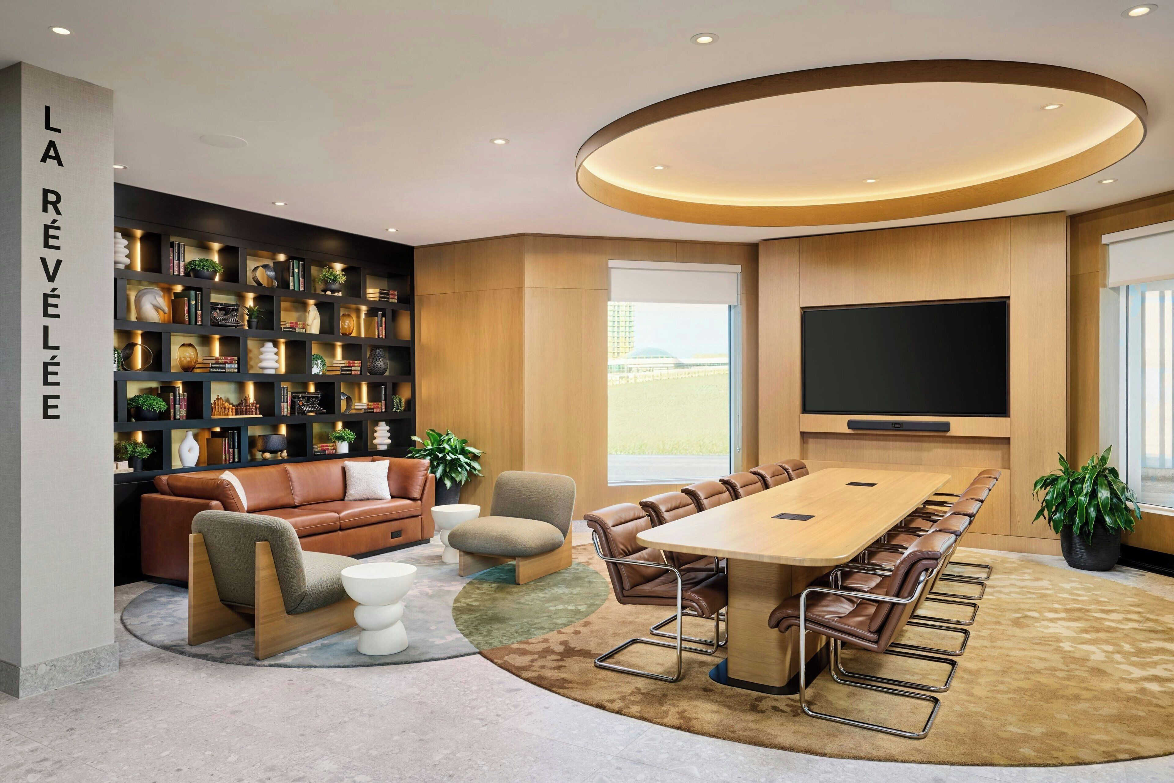 A modern conference room with a long table, leather chairs, a sofa, a bookshelf, and a large TV.