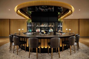 A circular bar area with a central bar, surrounded by six chairs, and shelves stocked with bottles and glasses. - Ômage Hotel, Montreal Laval, a Tribute Portfolio Hotel (Laval)