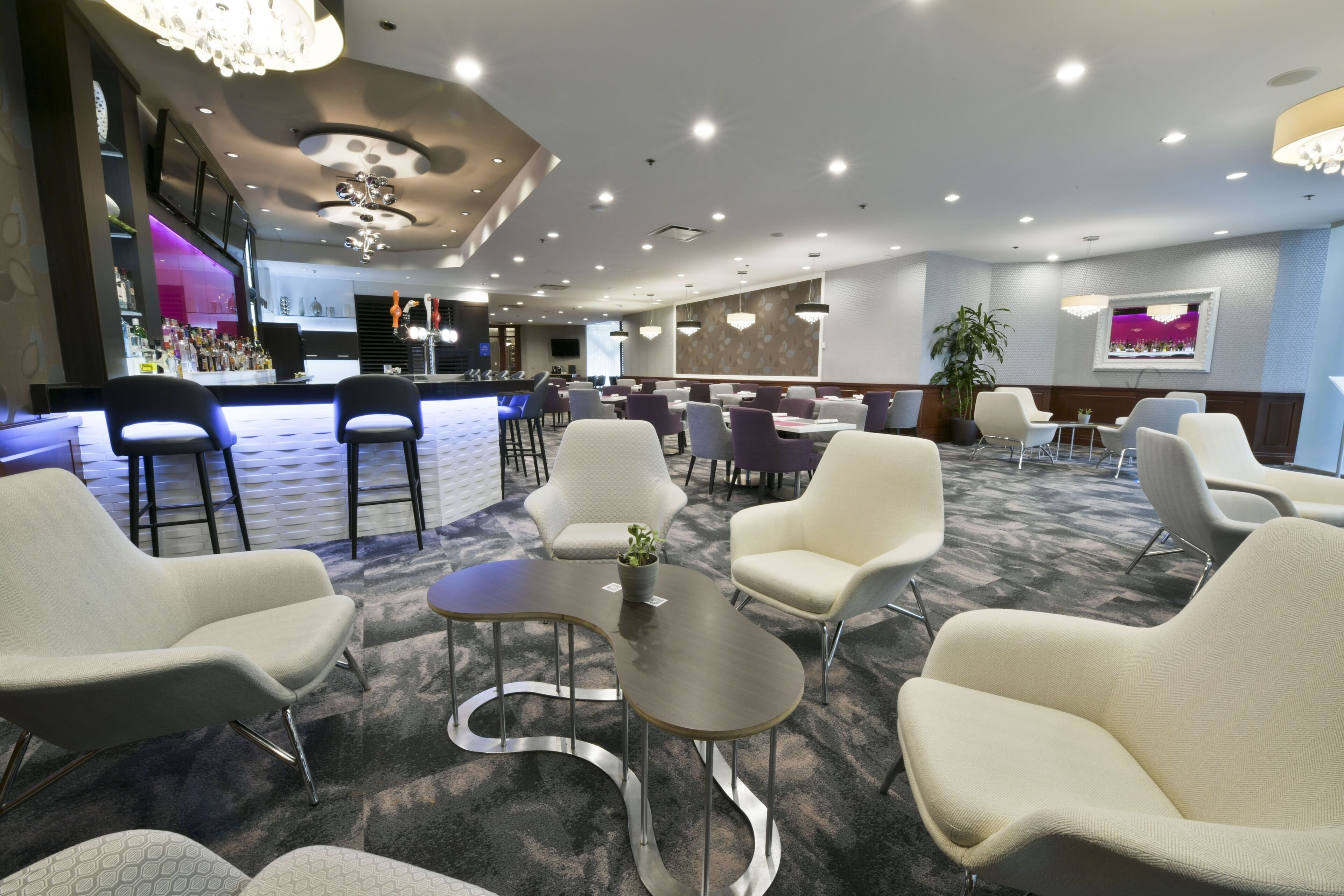 A modern hotel lobby with seating areas, a bar, and a large screen.