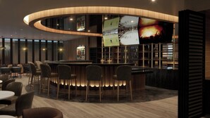 Zona de bar moderna con barra de madera curvada, diversas opciones de asiento y una pantalla grande mostrando deportes.