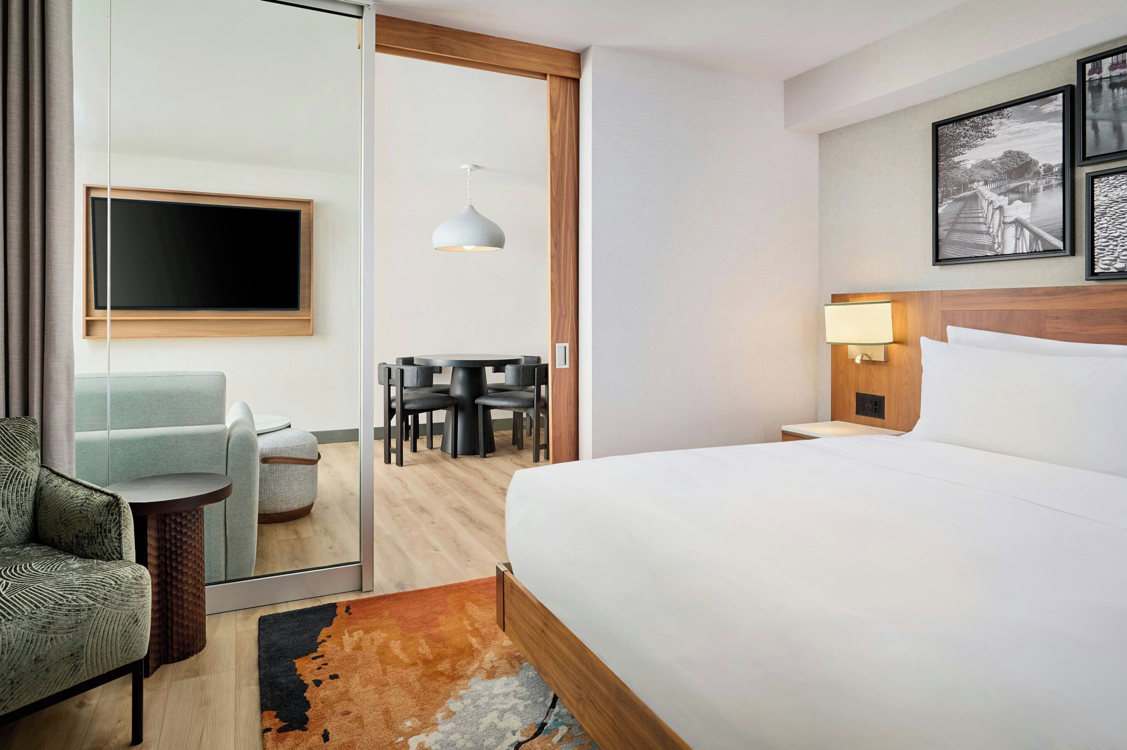 A hotel room with a bed, a TV, a desk with chairs, and a dining table.