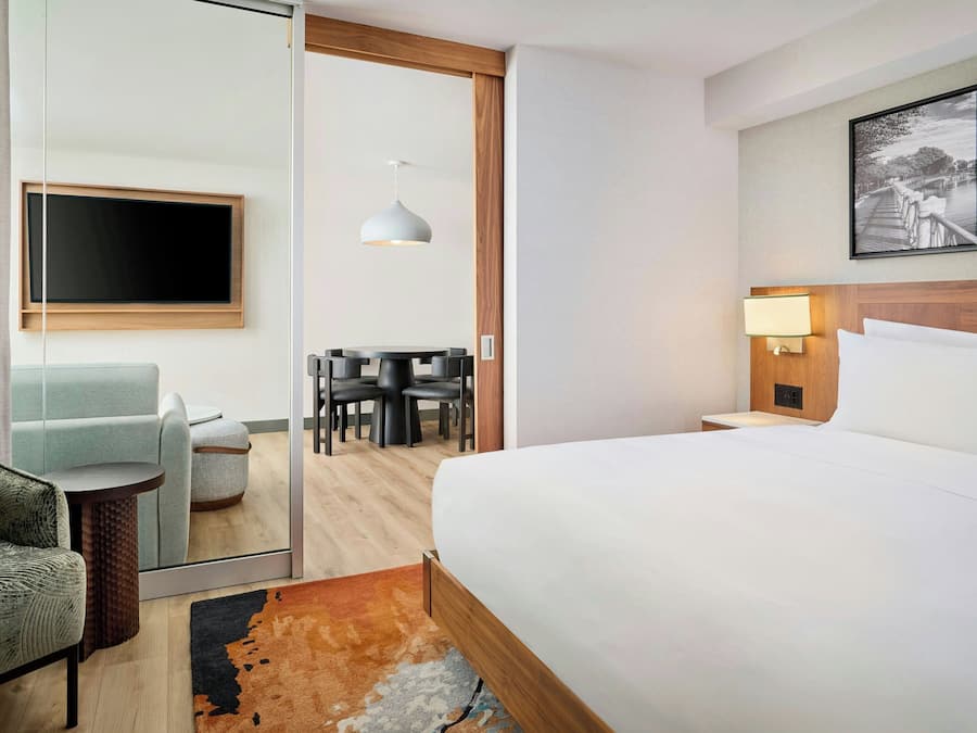 A hotel room with a bed, a TV, a desk with chairs, and a dining table.