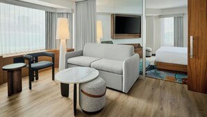 Habitación de hotel con sofá, dos sillones, una mesita, televisión, cama y puerta corredera.