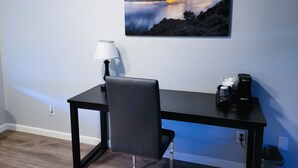 Ein Zimmer mit Schreibtisch, Stuhl, Lampe und einem Gemälde, das einen Sonnenuntergang über einem See zeigt.