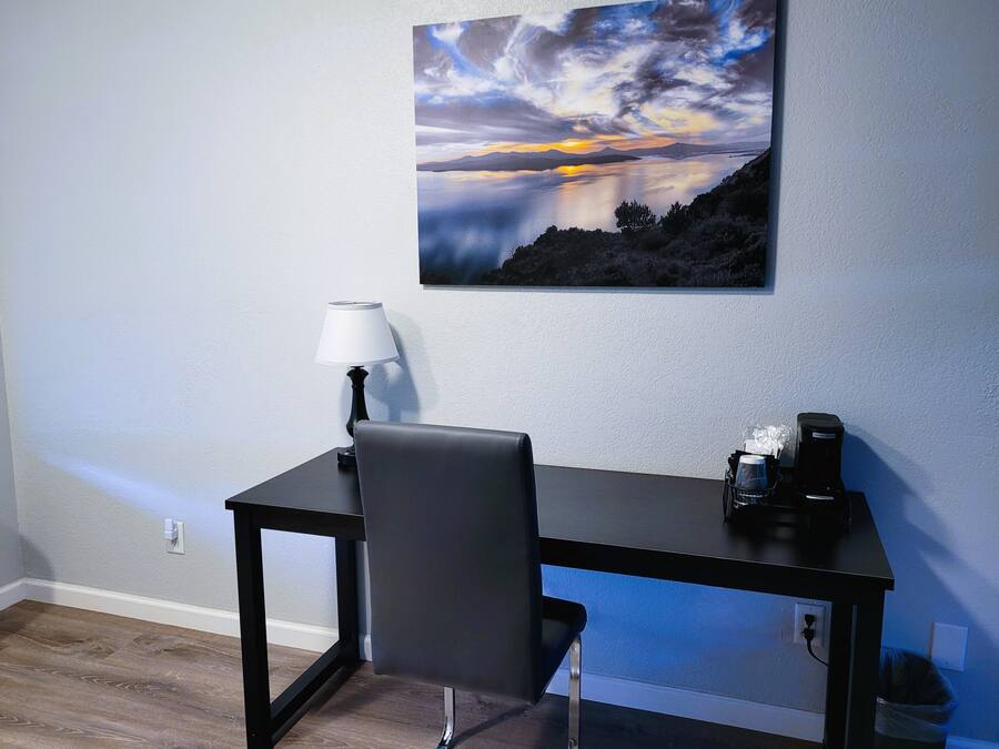 Ein Zimmer mit Schreibtisch, Stuhl, Lampe und einem Gemälde, das einen Sonnenuntergang über einem See zeigt.