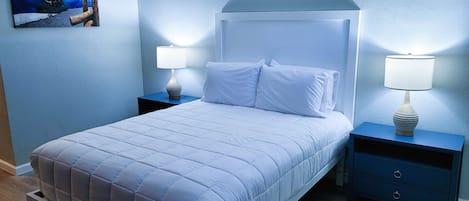 A neatly made bed with white bedding, two bedside tables with lamps, and a painting on the wall.