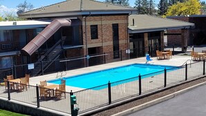 Ein Swimmingpool mit Rutsche, umgeben von einem Zaun, und Sitzgelegenheiten im Freien.