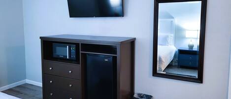 A hotel room with a bed, a dresser with a microwave, a TV, a mirror, and a trash can.