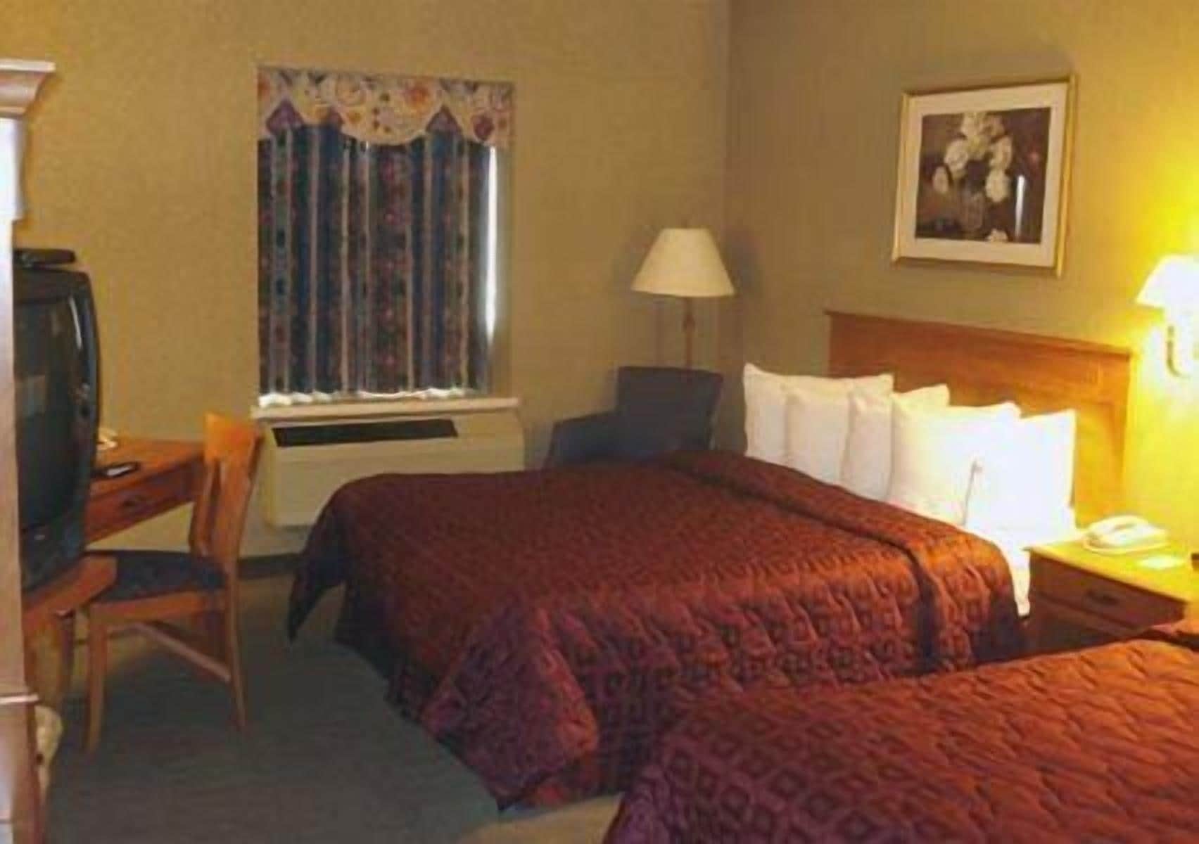 A hotel room with a bed, a desk, a chair, a lamp, and a television.