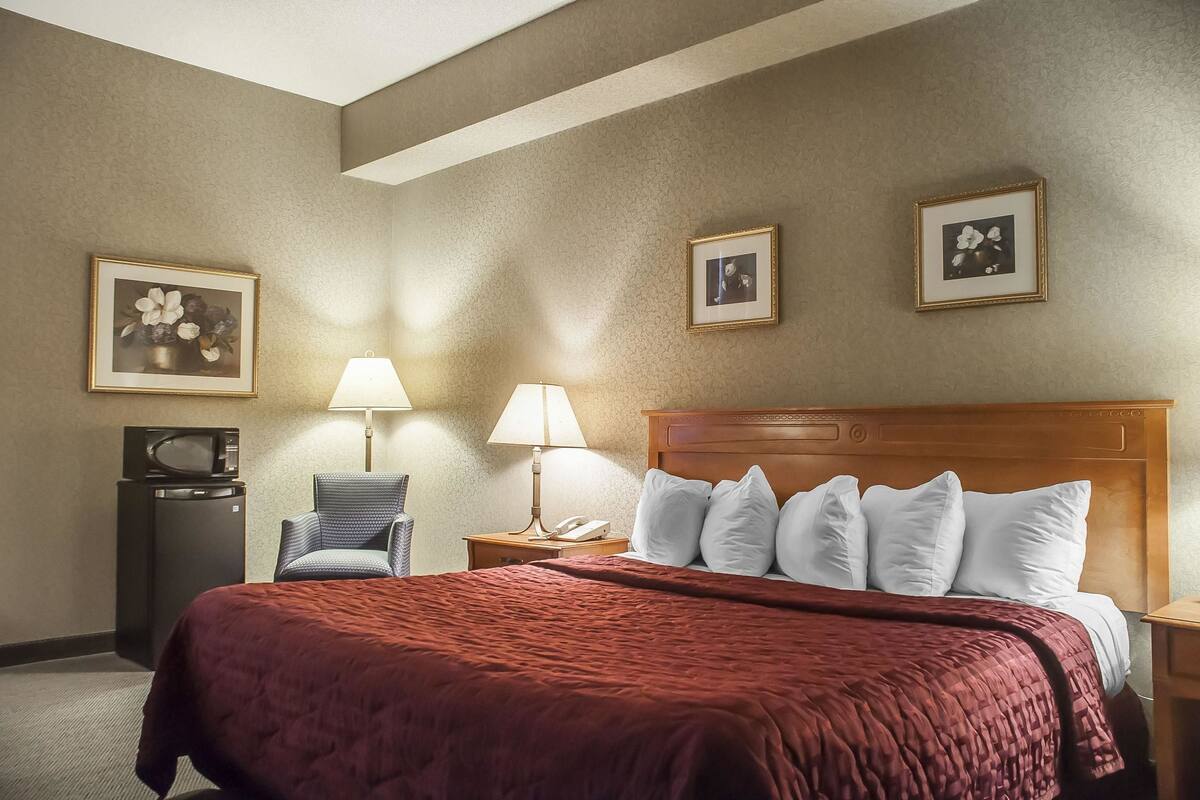A hotel room with a large bed, a television, a chair, and two lamps.