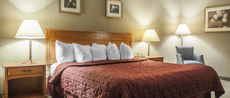 A hotel room with a large bed, two bedside lamps, a wooden nightstand, and a chair.