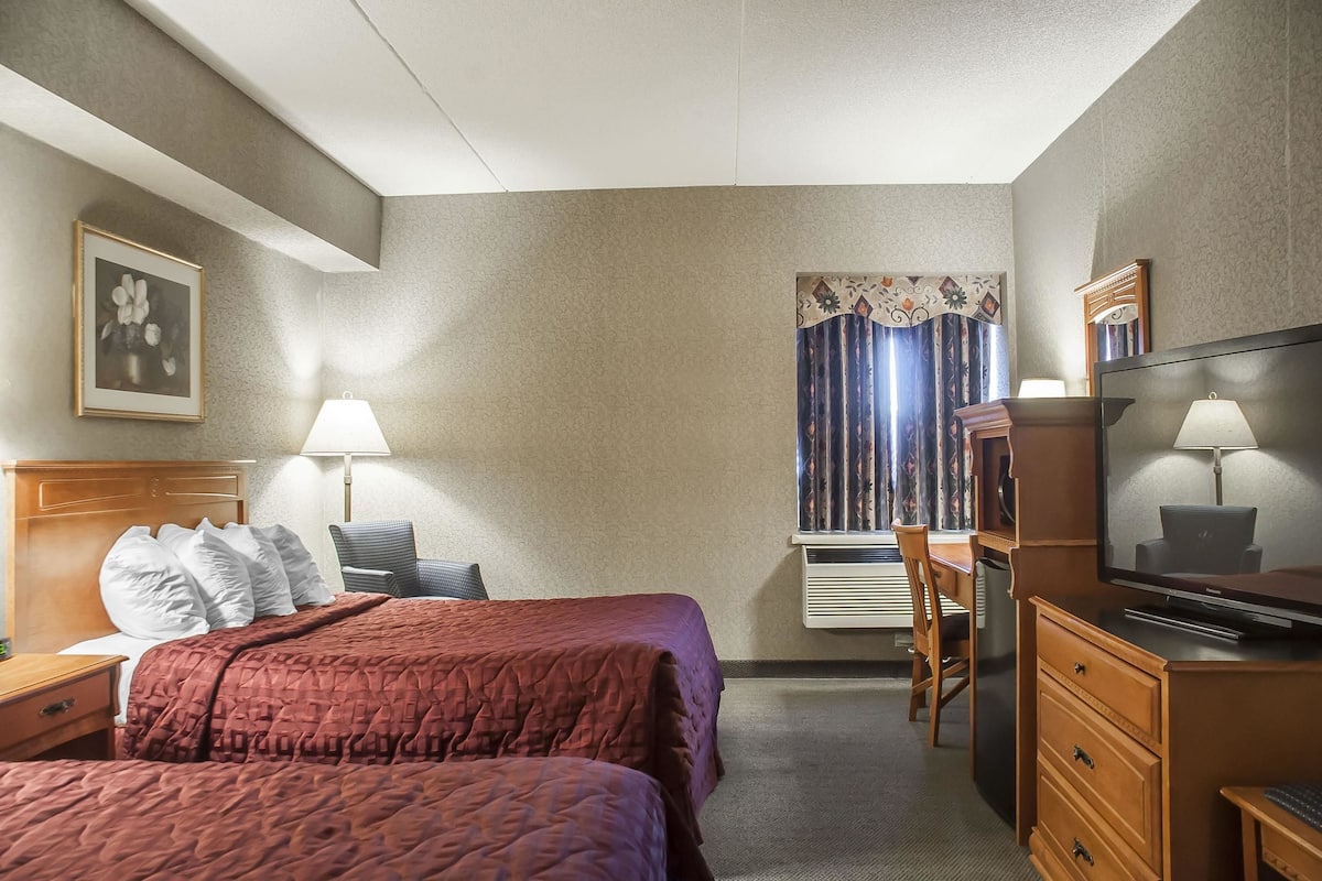 A hotel room with two beds, a desk, a dresser, a television, and a window with curtains.