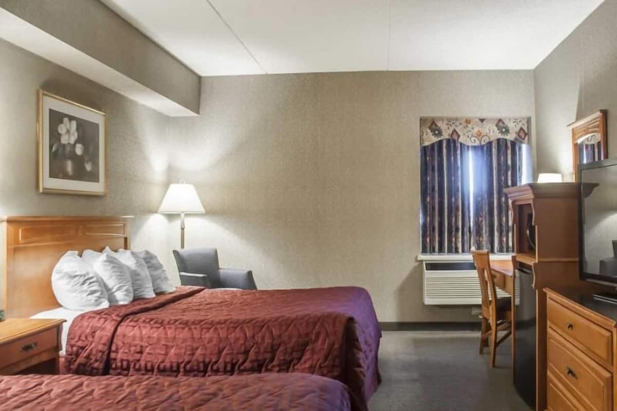 A hotel room with a bed, a desk, a chair, a lamp, and a window with curtains.