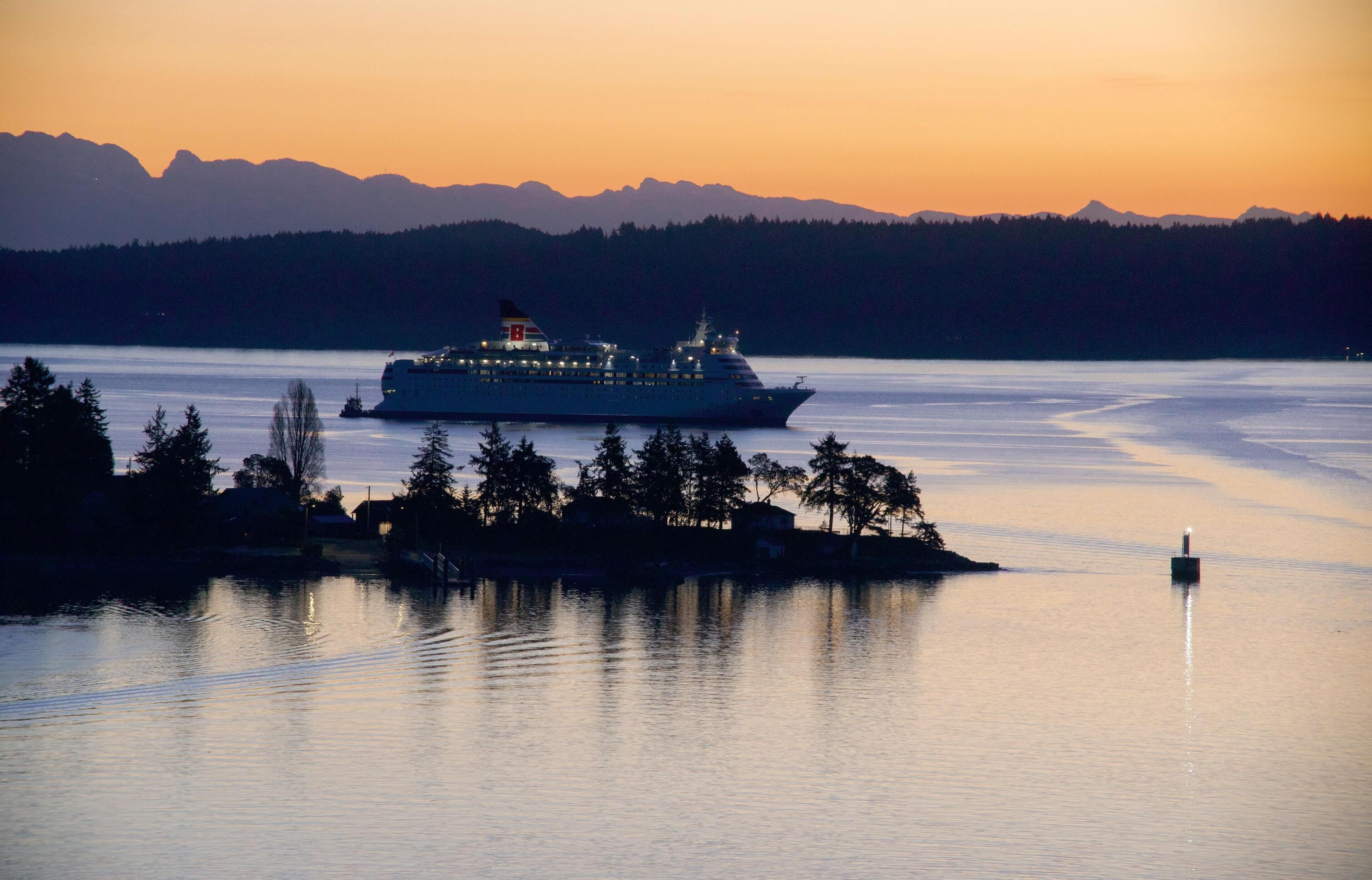 A cruise ship at sunset with mountains in the background.