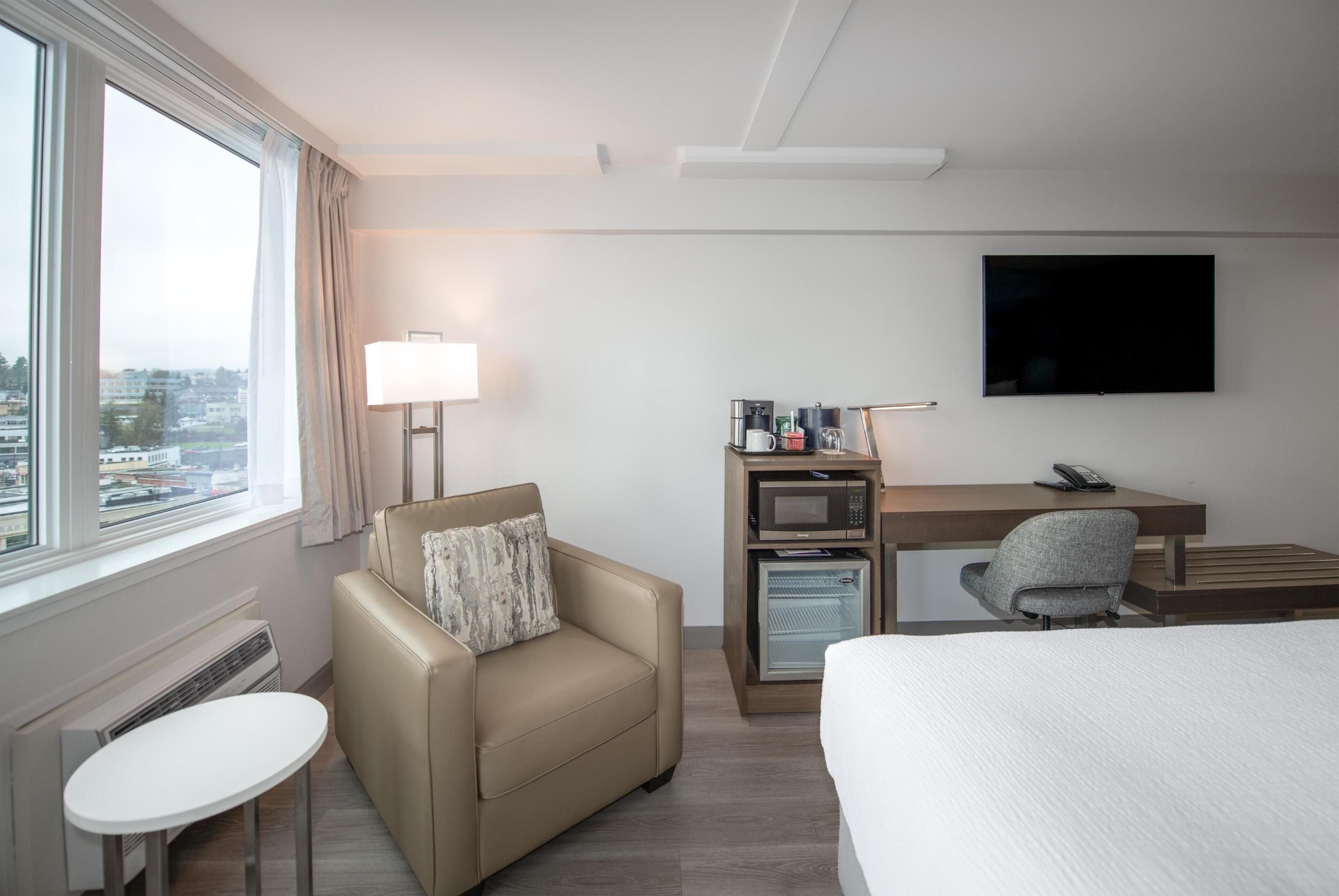 A hotel room with a bed, a desk with a computer and a lamp, a small table, and a sofa.