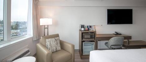 A hotel room with a bed, a desk with a computer and a lamp, a small table, and a sofa.