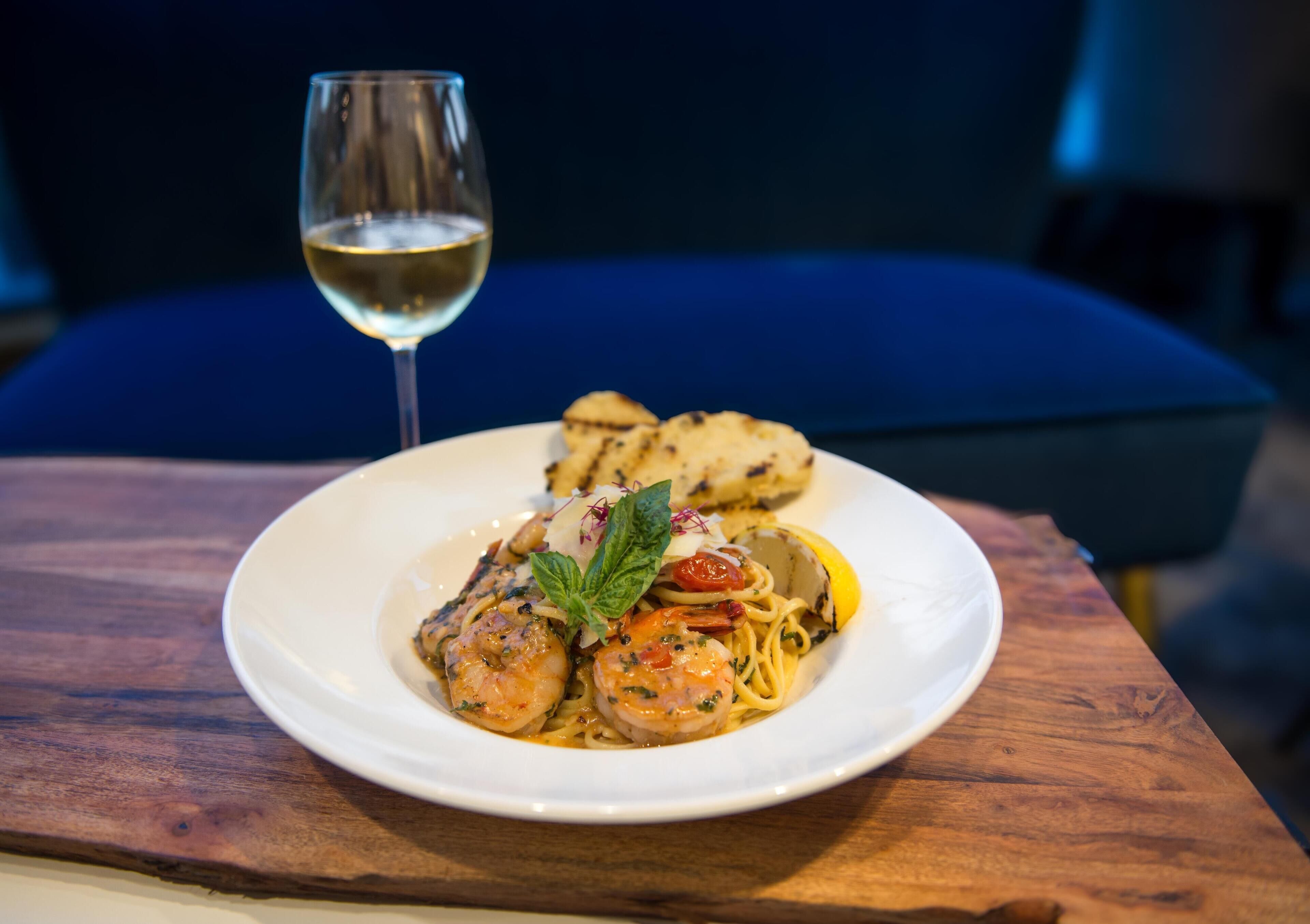 A plate of pasta with shrimp and lemon on a wooden table.