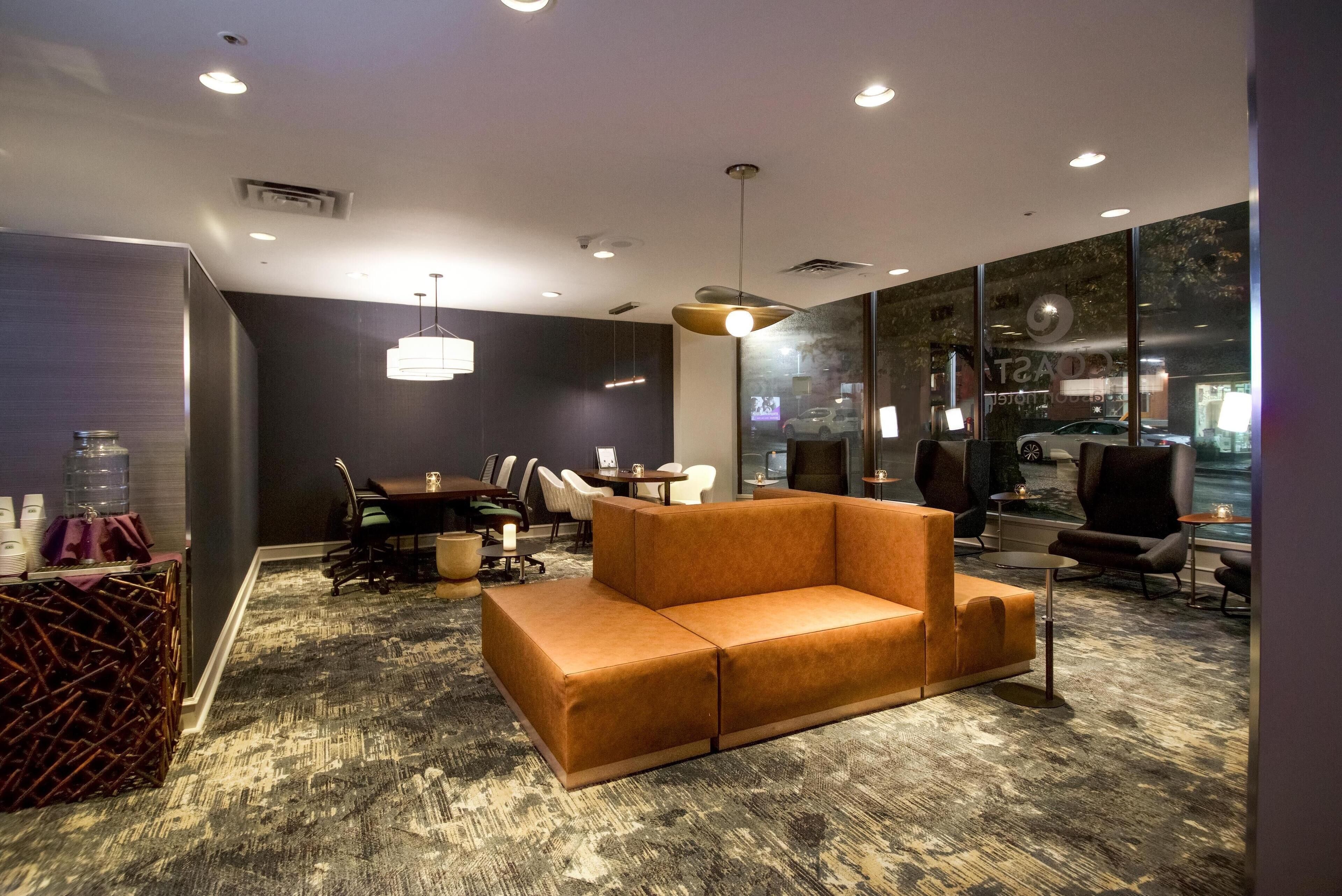 A modern lounge area with a sectional sofa, a dining table with chairs, and a large window providing a view of parked cars.