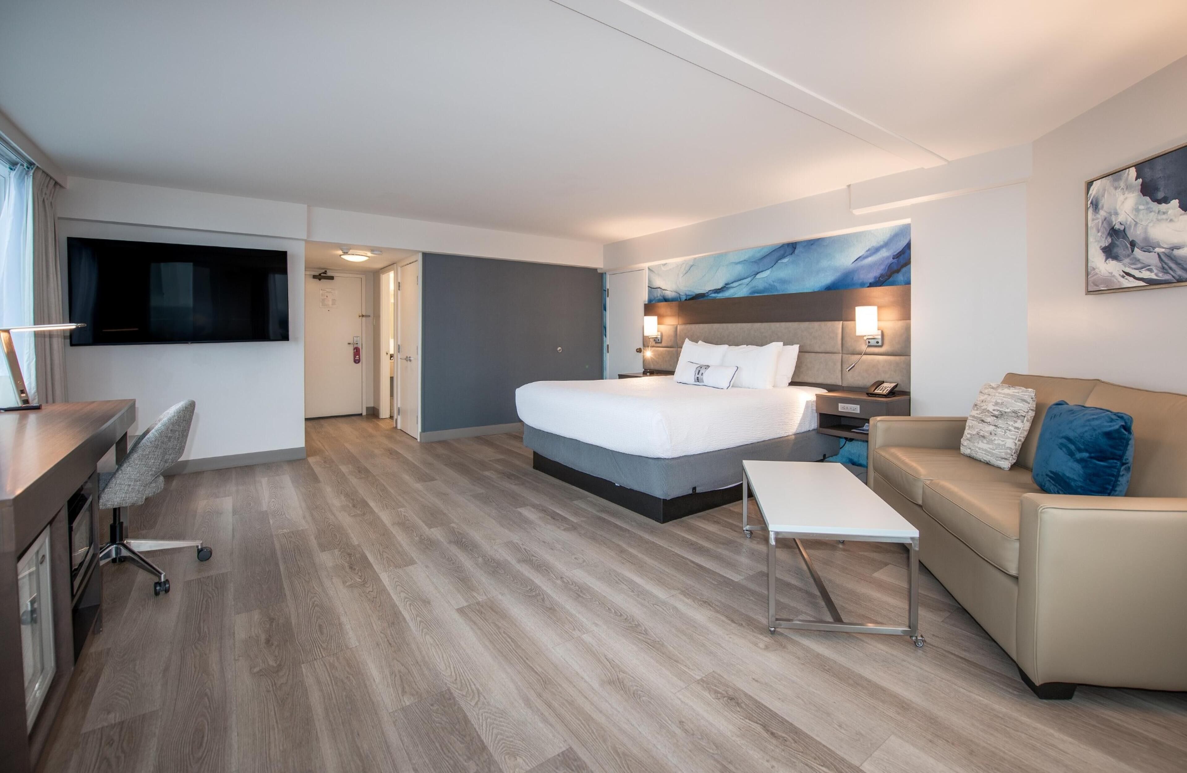 Una habitación de hotel moderna con una cama grande, un sofá, un escritorio con silla, un televisor de pantalla plana y obras de arte en las paredes.