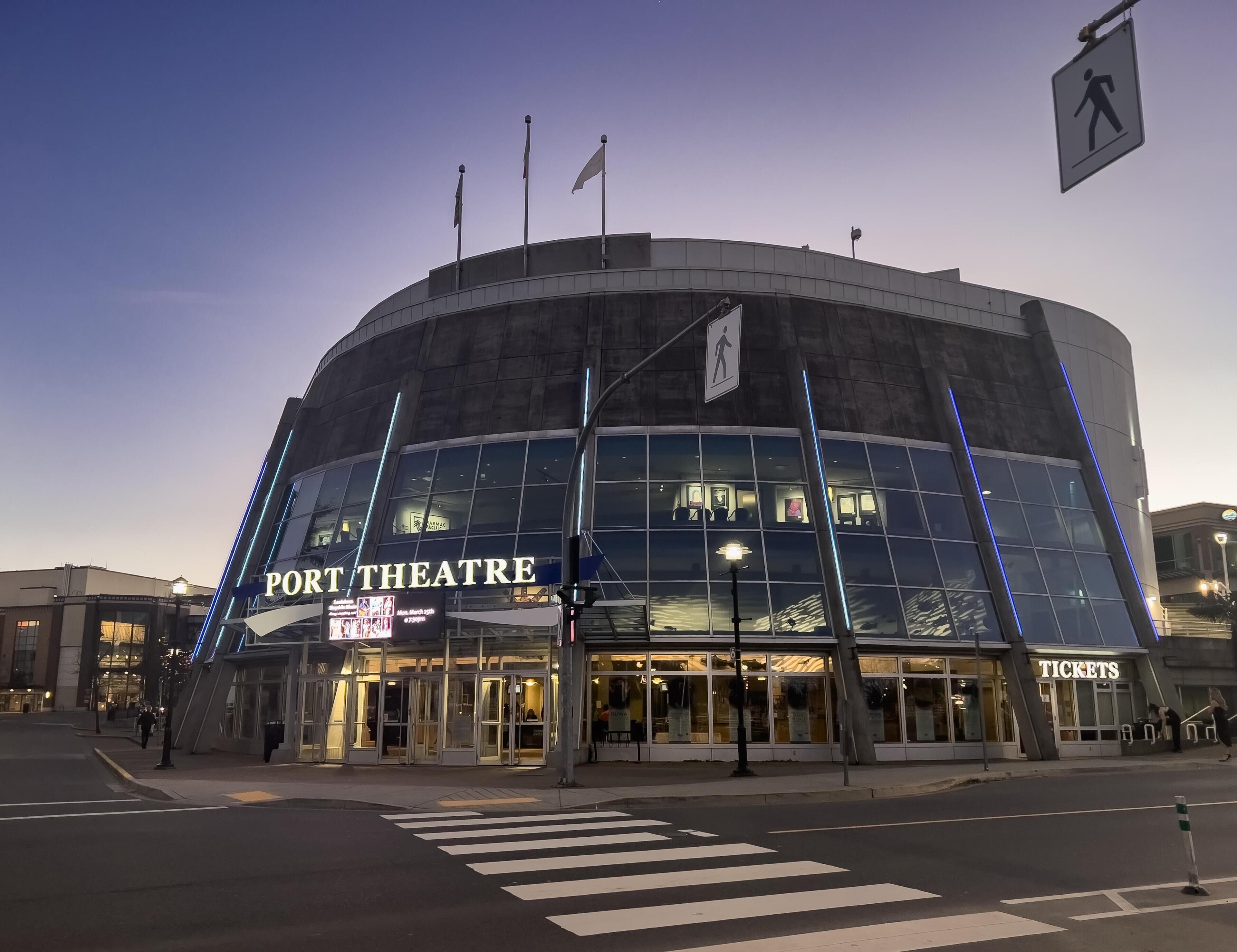 A modern theater building with a large glass facade, a ticket booth, and a pedestrian crossing.