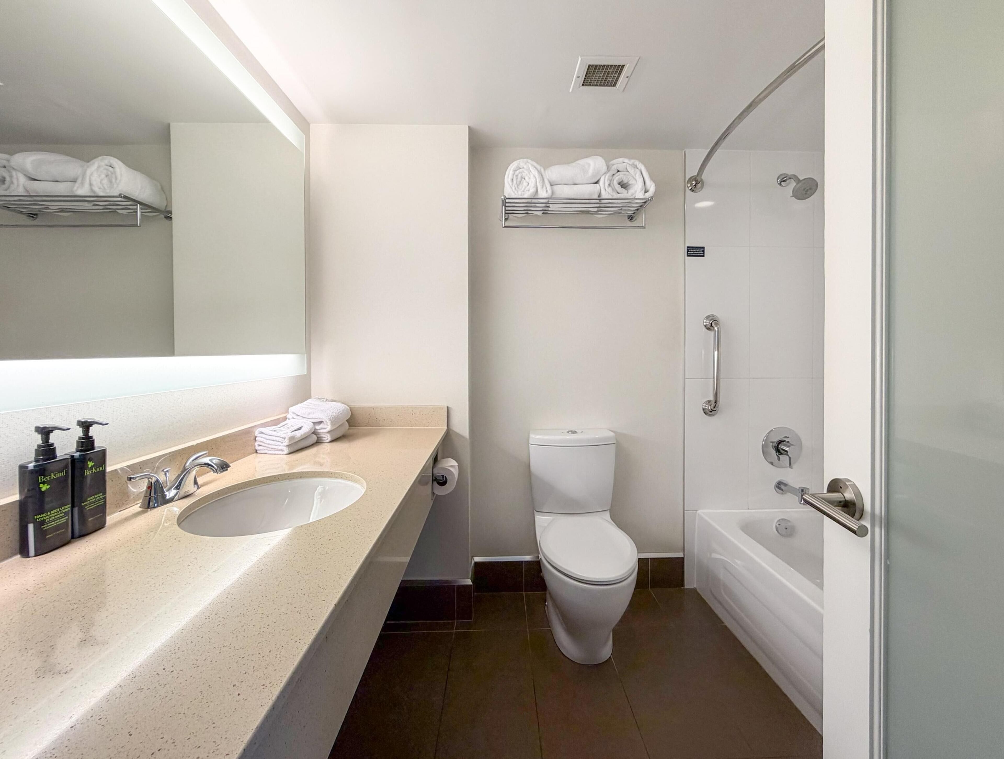 Un baño moderno con lavamanos, inodoro y ducha. Hay toallas en un estante sobre el inodoro y un secador de manos al lado del lavamanos.