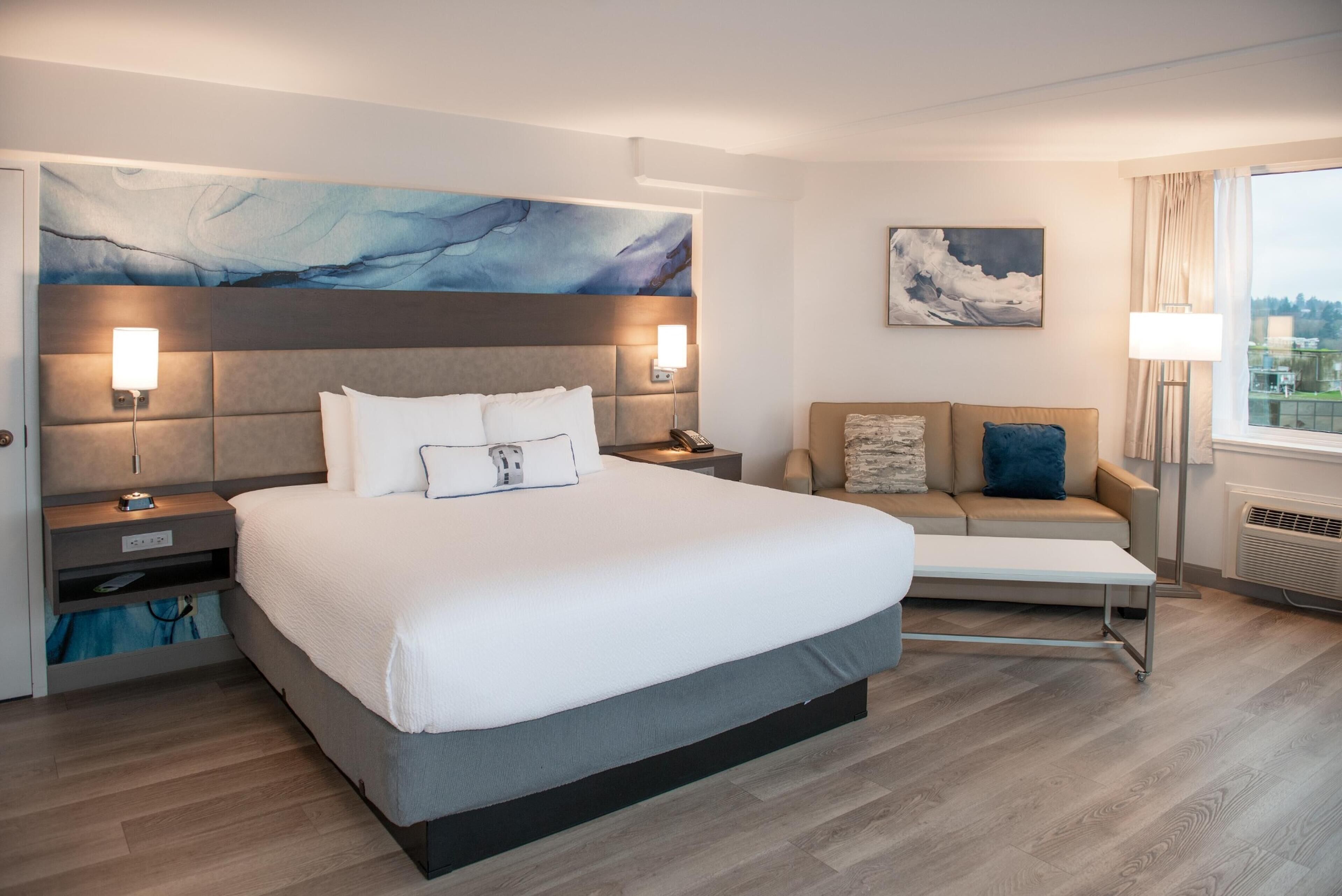 Une chambre d’hôtel moderne avec un grand lit, un canapé, un tableau et une vue sur la ville.