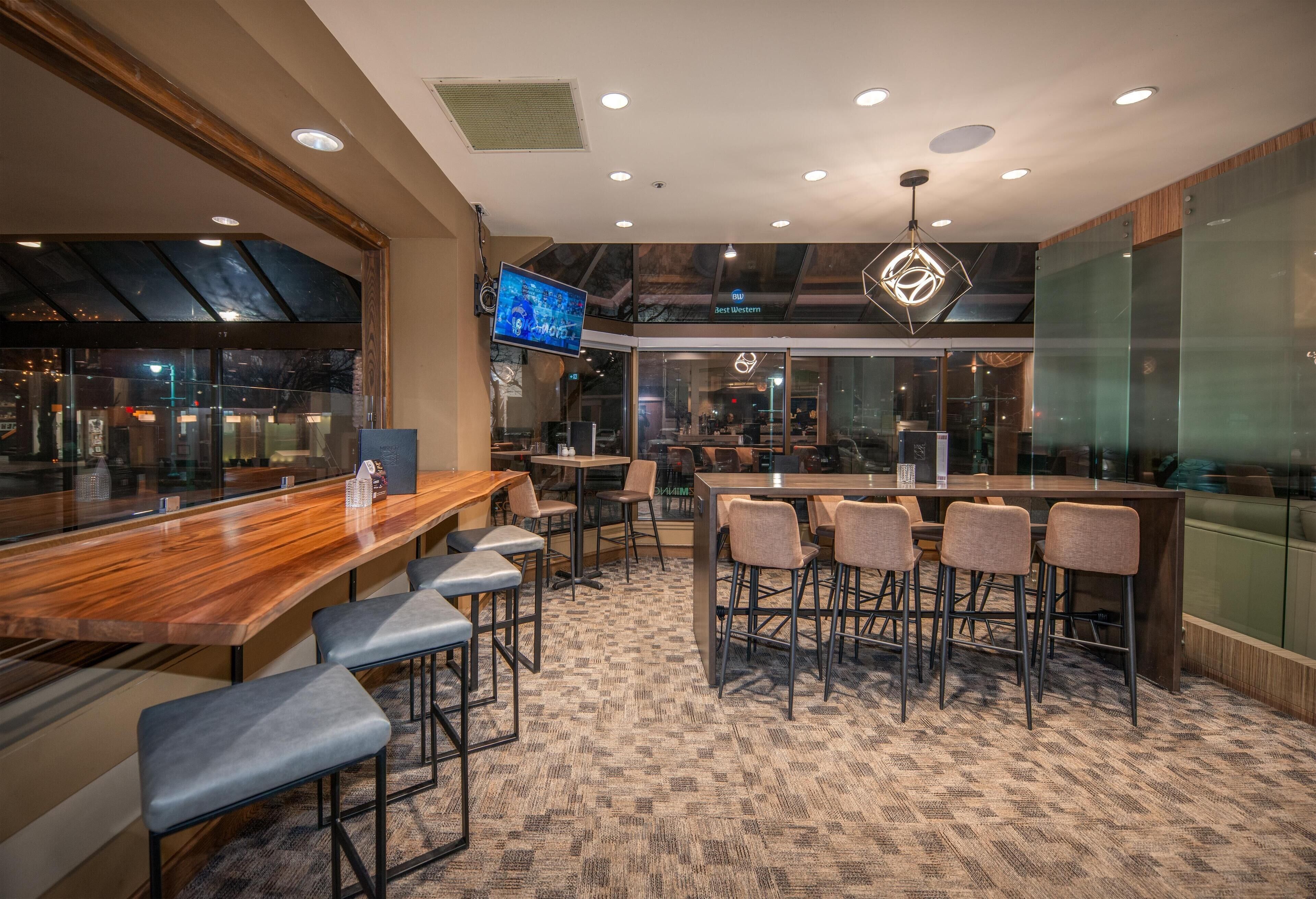 Un área de bar moderna con una barra de madera, taburetes y una pantalla grande.