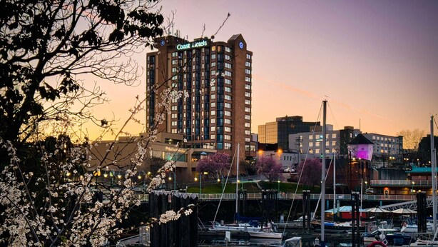 Un puerto deportivo con barcos amarrados, un edificio con el letrero 'Coast Hotels' y flores de cerezo al frente.