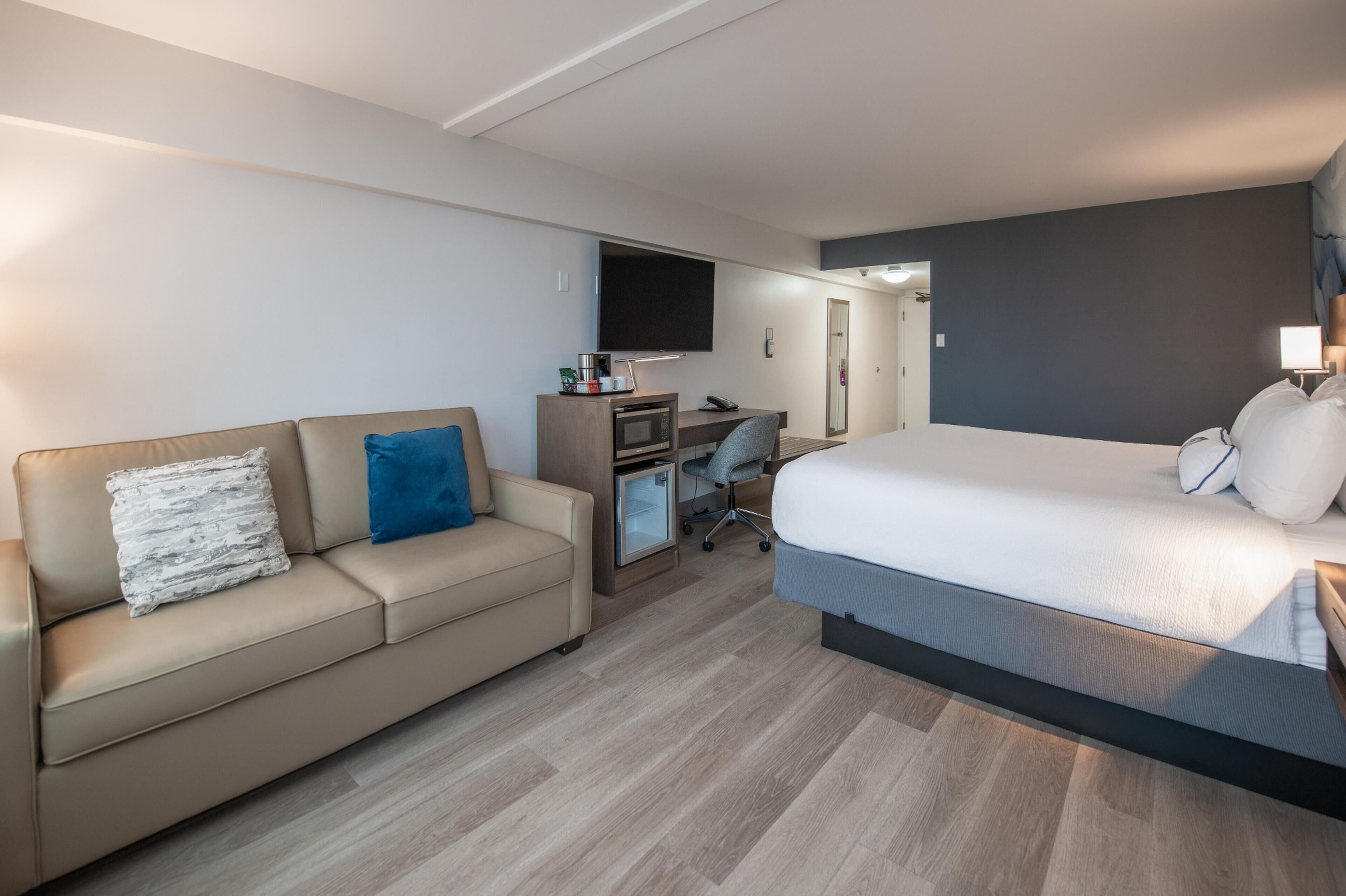 A hotel room with a bed, a sofa, a desk with a computer, and a TV.