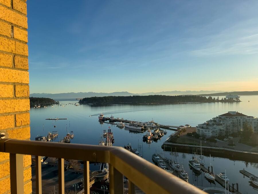 A marina with boats docked, a cruise ship in the distance, and a view of the surrounding landscape.