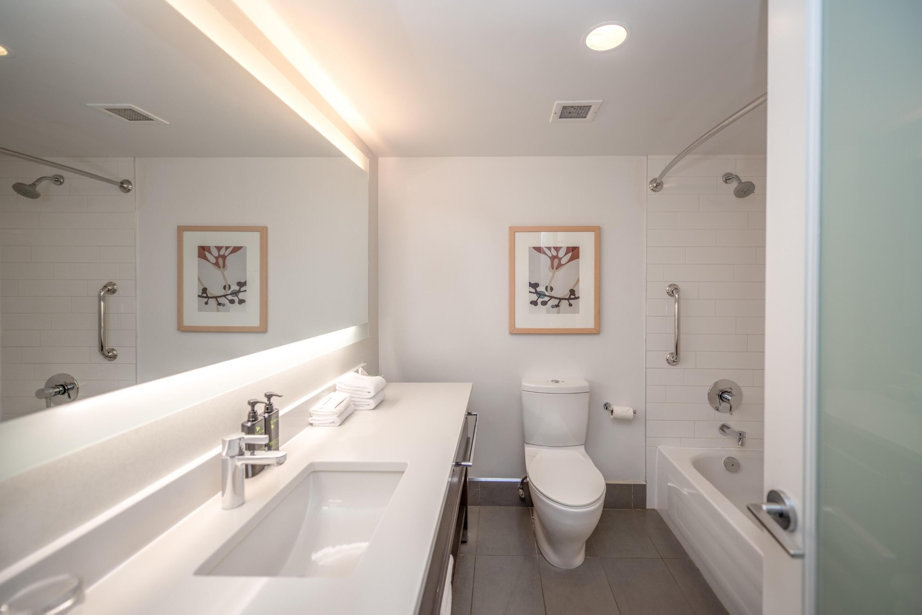 Een moderne badkamer met een grote spiegel, een wastafel, een toilet en een bad.
